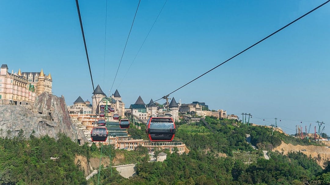 Cable cars traveling to Ba Na Hills in Da Nang, Vietnam with castle-like structures in view.