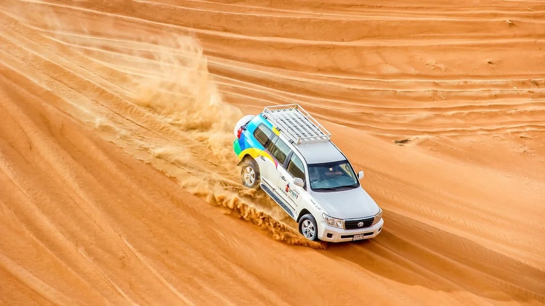 SUV driving through desert dunes during sunrise safari.