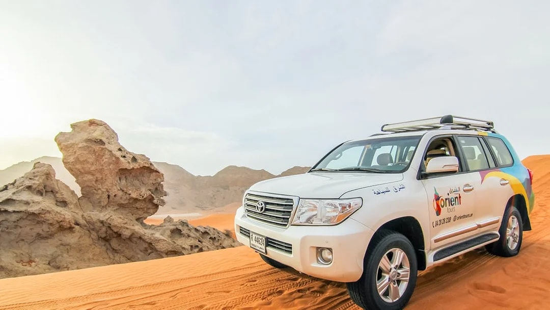 SUV on desert dunes during sunrise, part of a Sunrise Desert Safari with Picnic Breakfast.