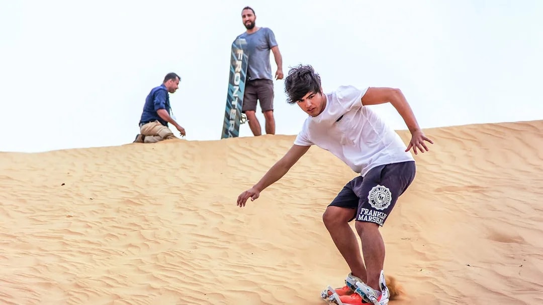 Sandboarding during sunrise desert safari with picnic breakfast.