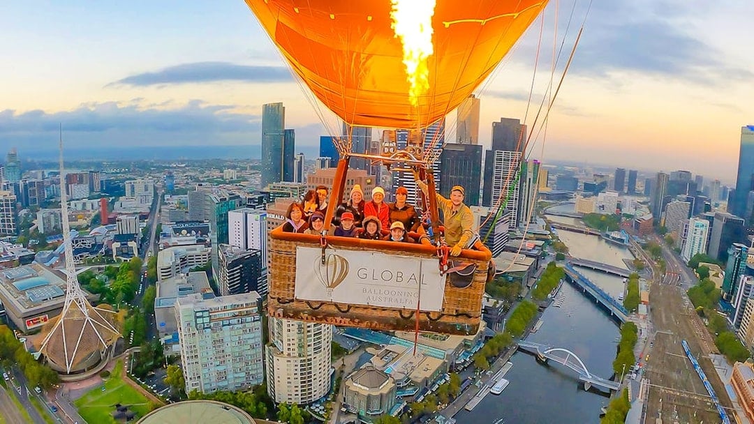 Hot air balloon over Melbourne cityscape at sunrise.