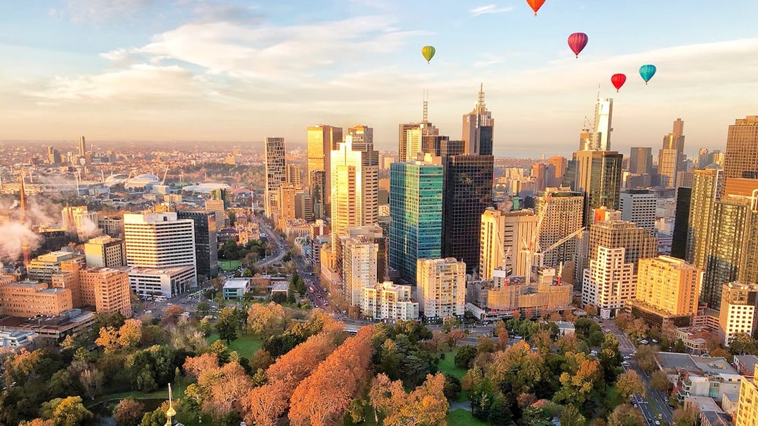Hot air balloons over Melbourne skyline at sunrise.