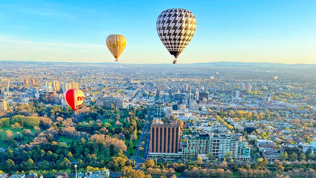 Hot air balloons floating over Melbourne cityscape at sunrise.