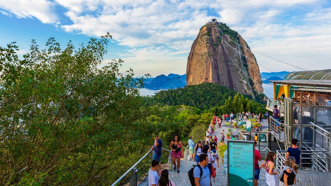Visitors at Sugarloaf Mountain, Rio de Janeiro, with cable car and scenic views.