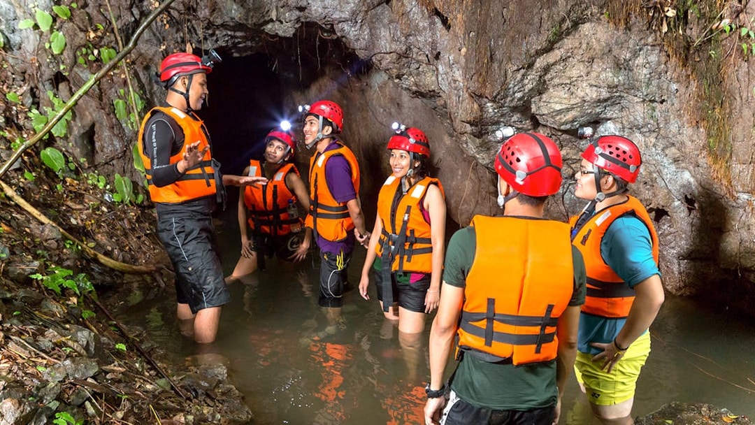 Group exploring cave in water at Sunway Lost World of Tambun, Malaysia, wearing helmets and life vests.