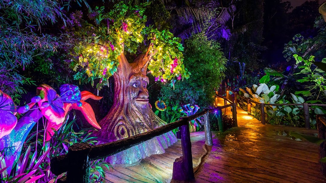Illuminated tree sculpture and vibrant plants at Lost World Hot Springs Night Park.