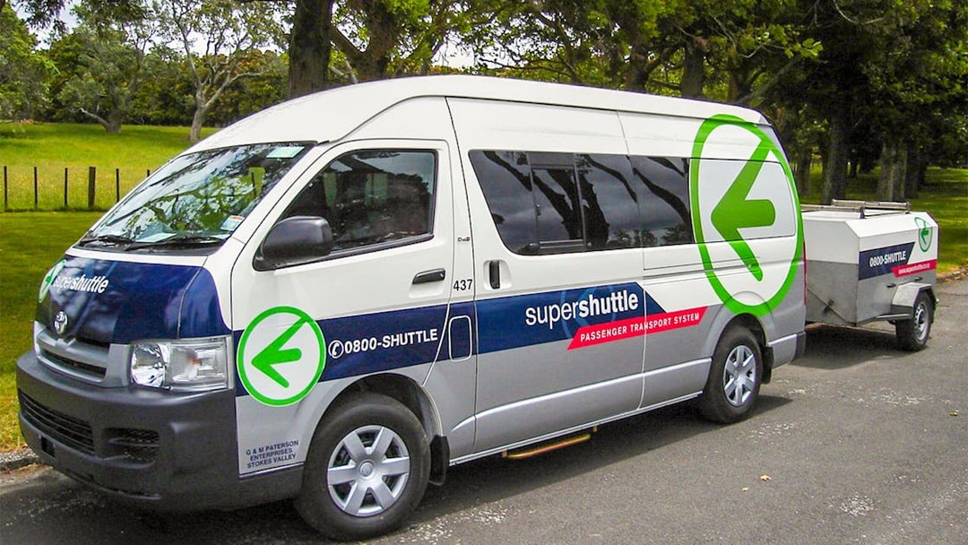 Super Shuttle van parked in a green area, used for airport transfers.