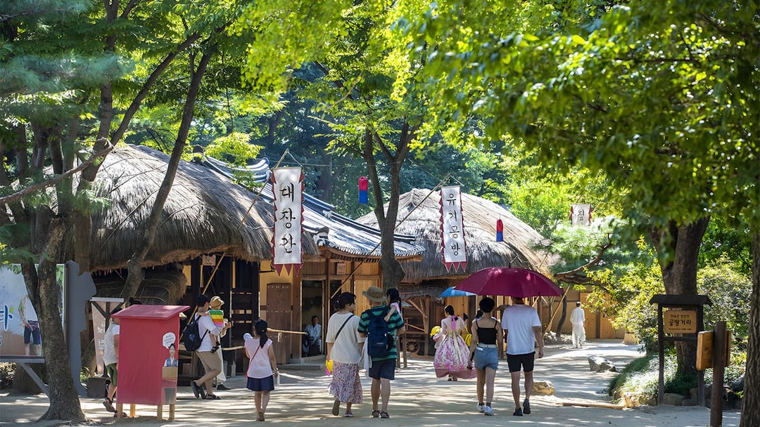 Visitors walking through traditional Korean Folk Village with thatched-roof houses, Suwon Hwaseong tour.