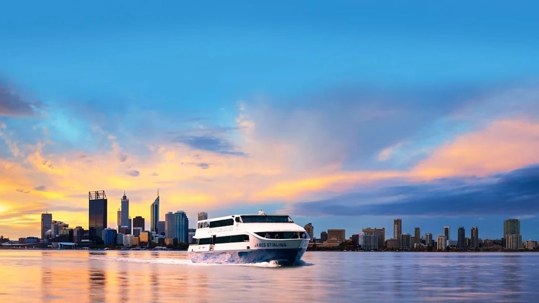 Cruise boat on Swan River with Perth city skyline at sunset.