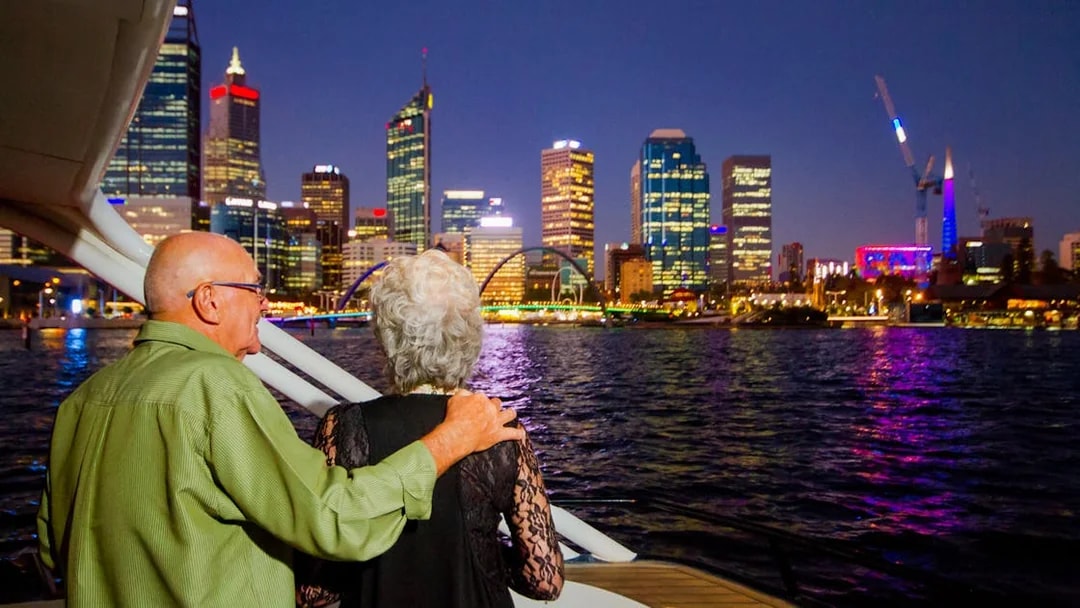 Elderly couple admiring city skyline from a cruise at night.
