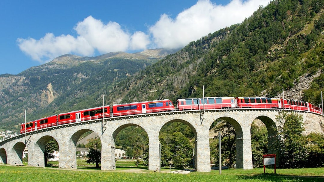 Bernina Express on Brusio Circular Viaduct with mountain backdrop.