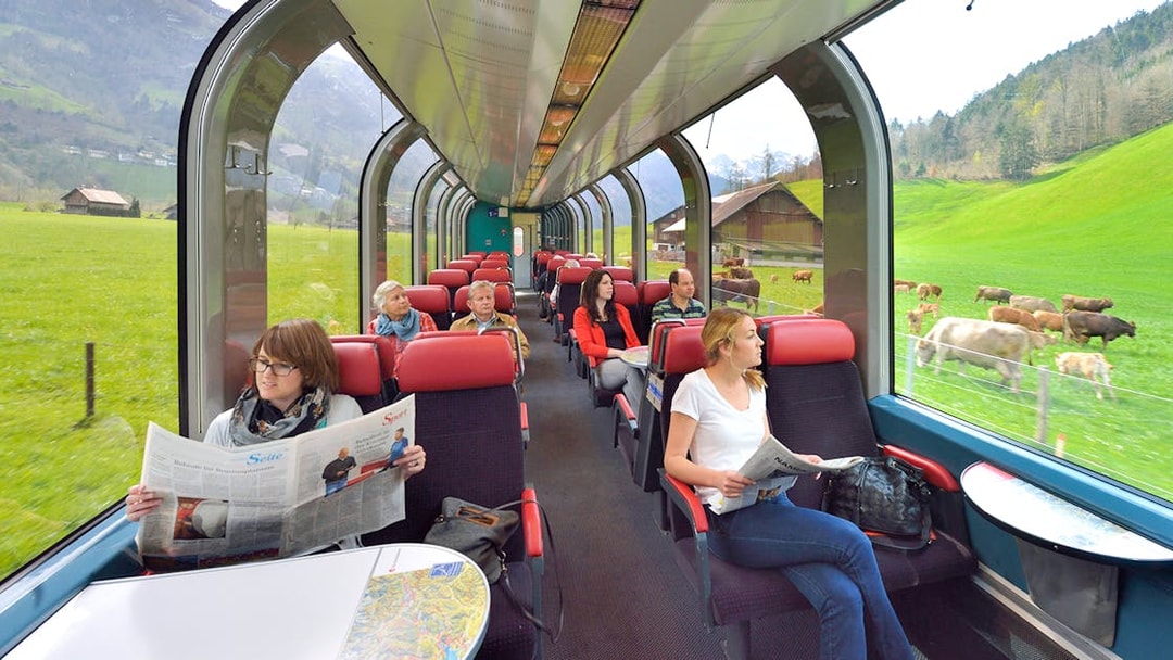 Passengers enjoying scenic view from panoramic train window in Swiss countryside.