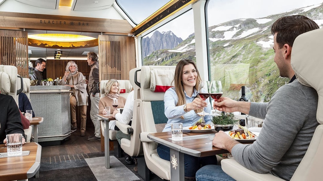 Passengers enjoying a meal and wine on a scenic Swiss train journey.