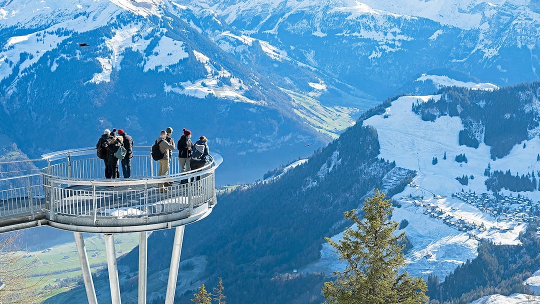 Visitors on Stanserhorn viewing platform overlooking snowy Swiss Alps.