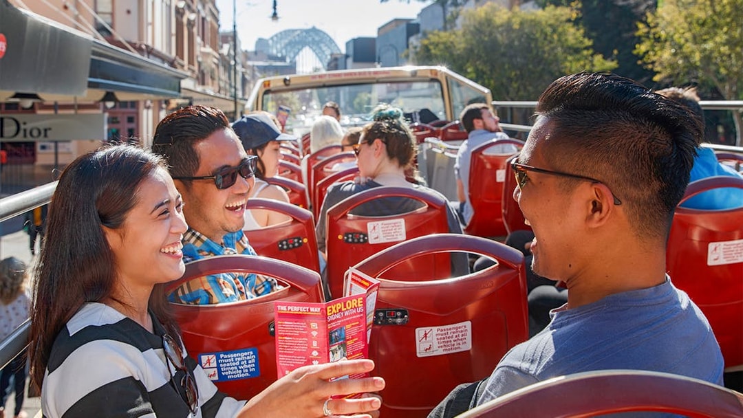 Passengers enjoying a ride on Big Bus Sydney with Sydney Harbour Bridge in the background.