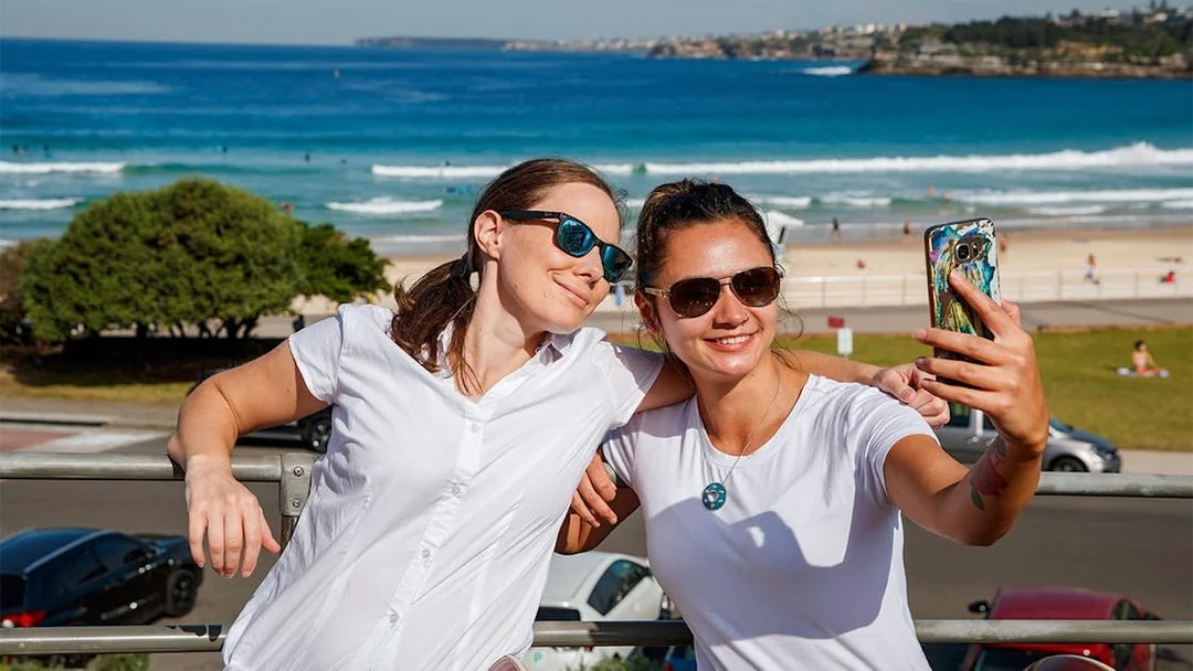 Passengers taking a selfie on Big Bus Sydney with Bondi Beach in the background.