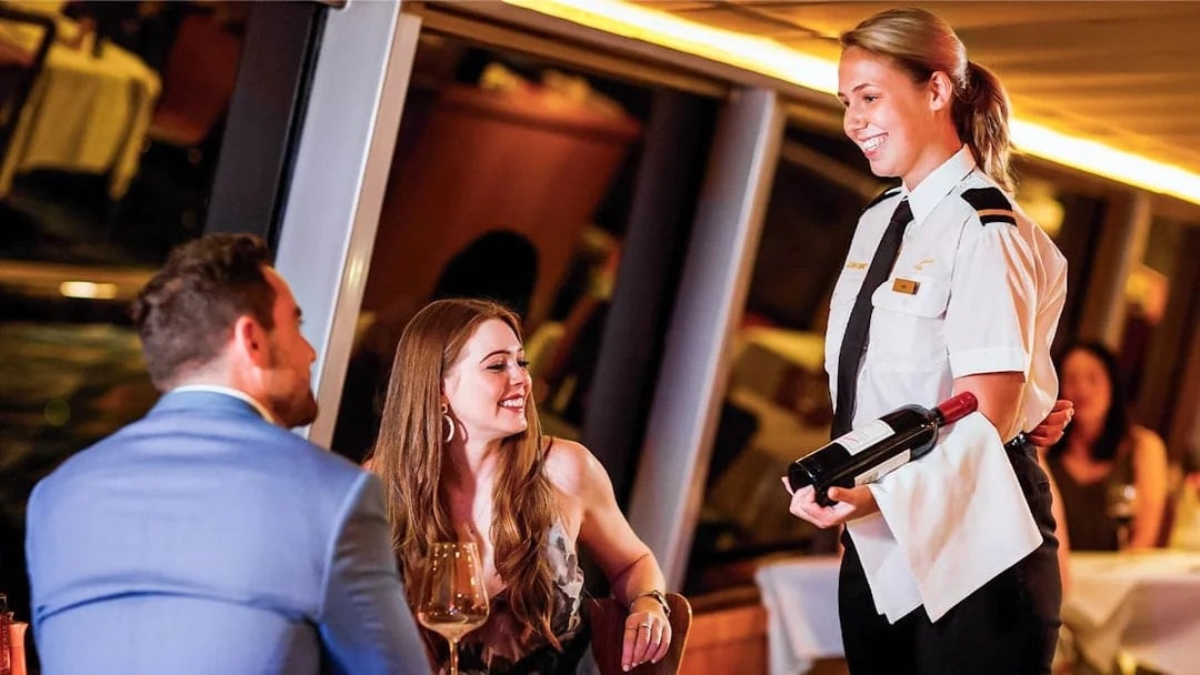 Couple dining on Sydney Harbour cruise with server presenting wine.