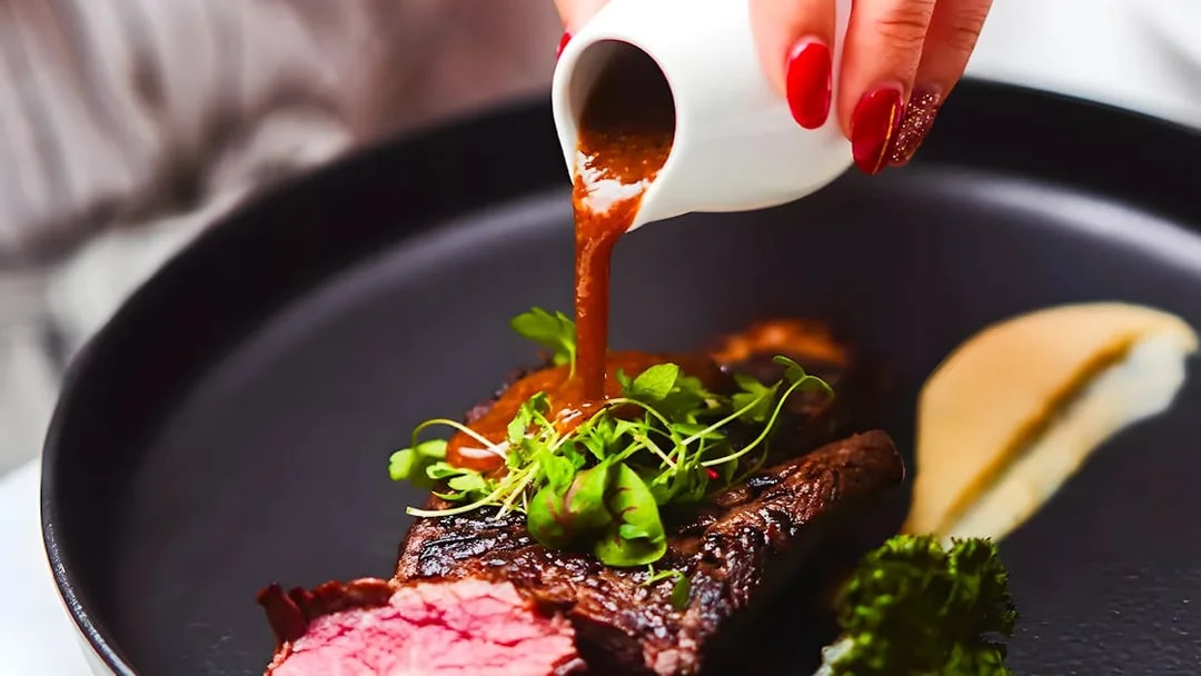 Steak with sauce being poured, garnished with greens, on the Gold Penfolds Dinner Cruise, Sydney Harbour.