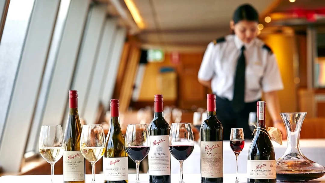 Penfolds wine bottles and glasses on a cruise dining table with a server in the background.