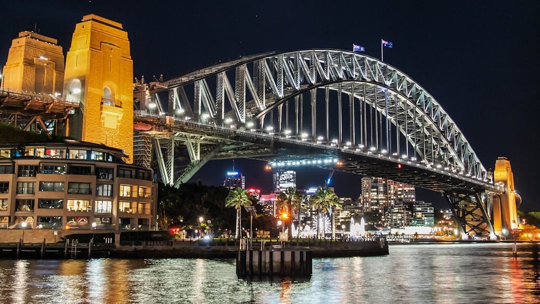 Sydney Harbour Bridge illuminated at night with city skyline in the background.
