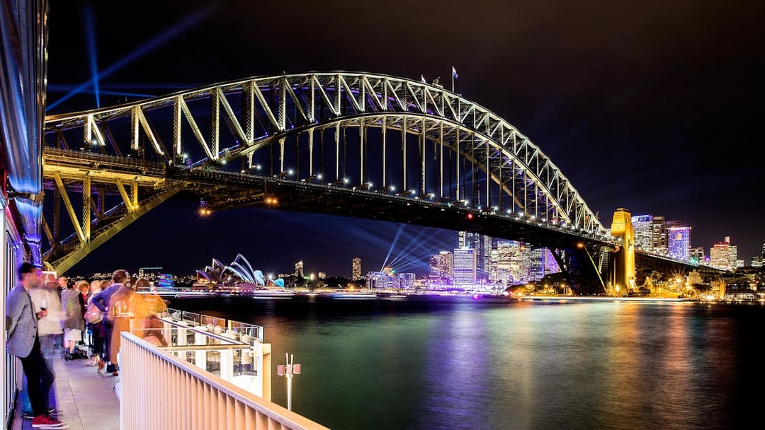 Sydney Harbour Bridge illuminated at night with city skyline and Opera House in view.