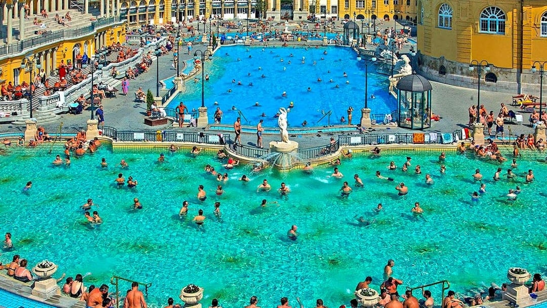 Outdoor pool at Széchenyi Thermal Bath, Budapest, with people swimming and relaxing.