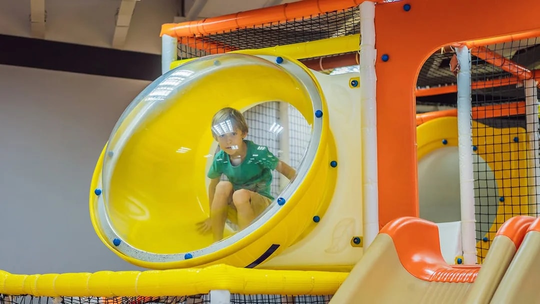 Child playing in a yellow tube slide at T-Play Khatib indoor playground.