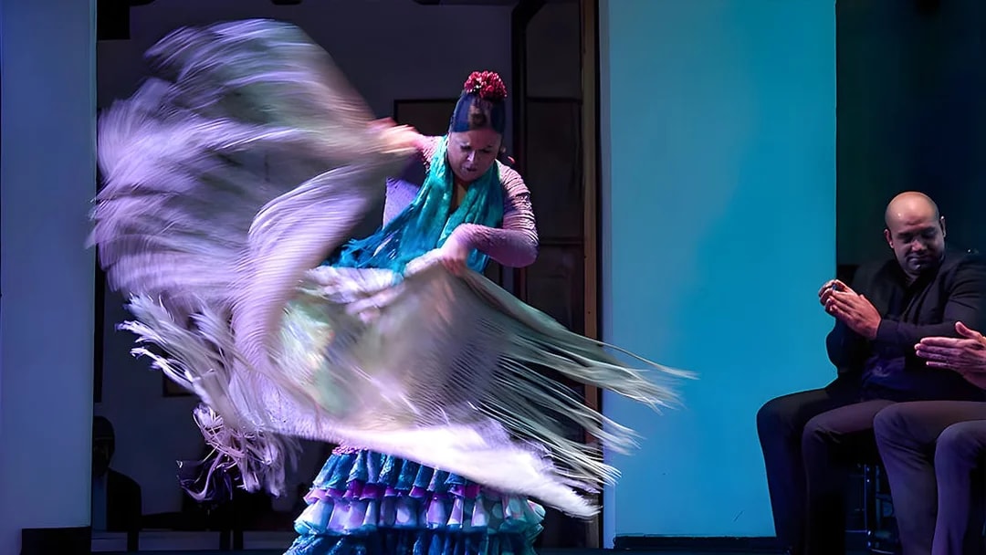 Flamenco dancer performing at Tablao El Arenal with musicians clapping.