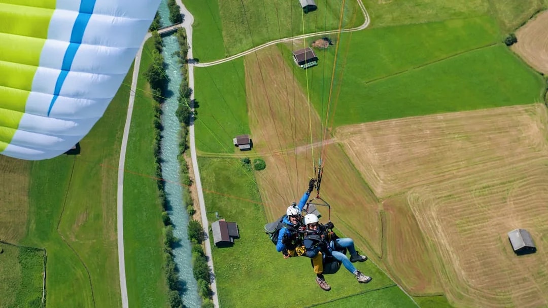 Tandem paragliding over green fields and river in Tirol, Austria.