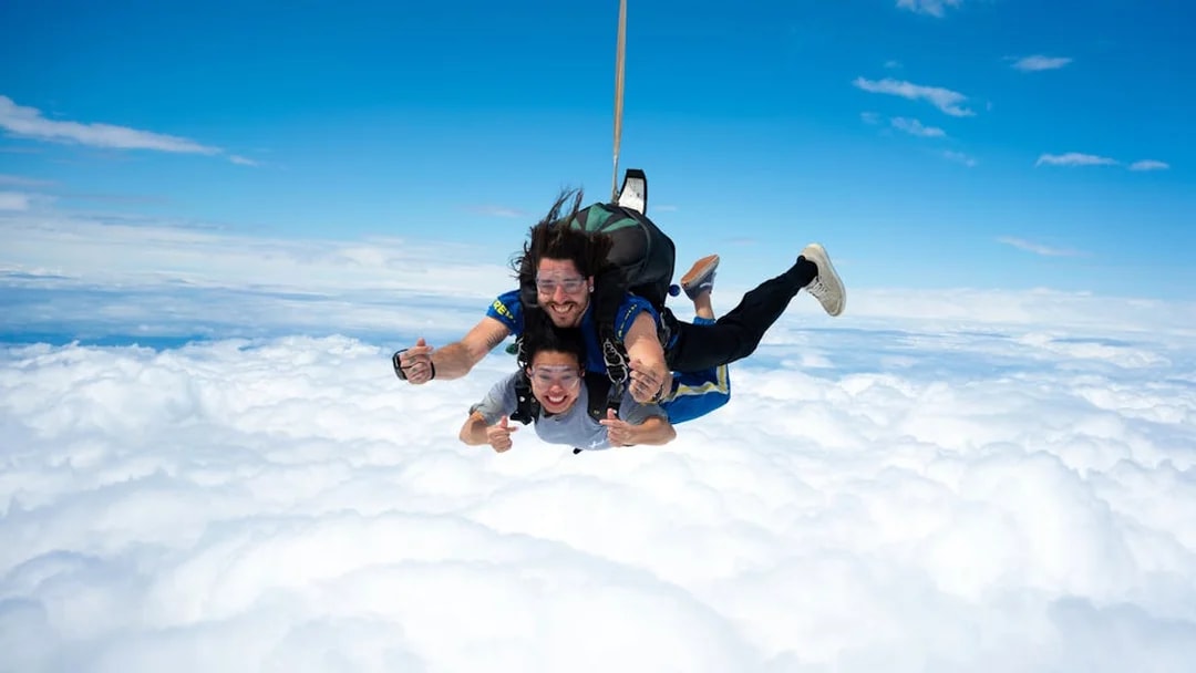 Tandem skydivers freefalling above clouds on Great Ocean Road.