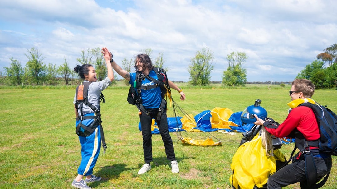 Skydivers celebrate landing on Great Ocean Road with parachutes in the background.