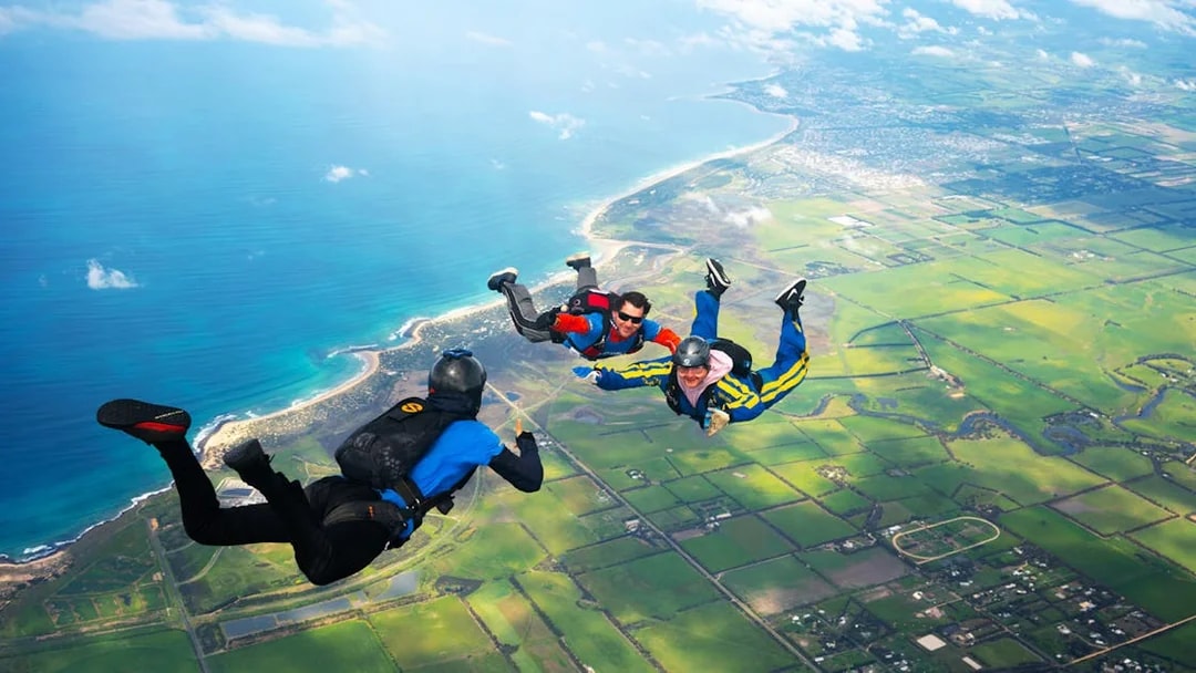 Skydivers tandem freefall over Great Ocean Road coastline, Australia.