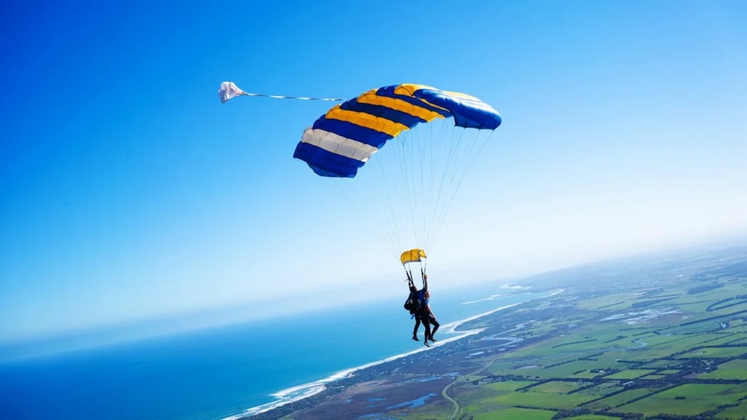 Skydivers tandem freefall over Great Ocean Road coastline.