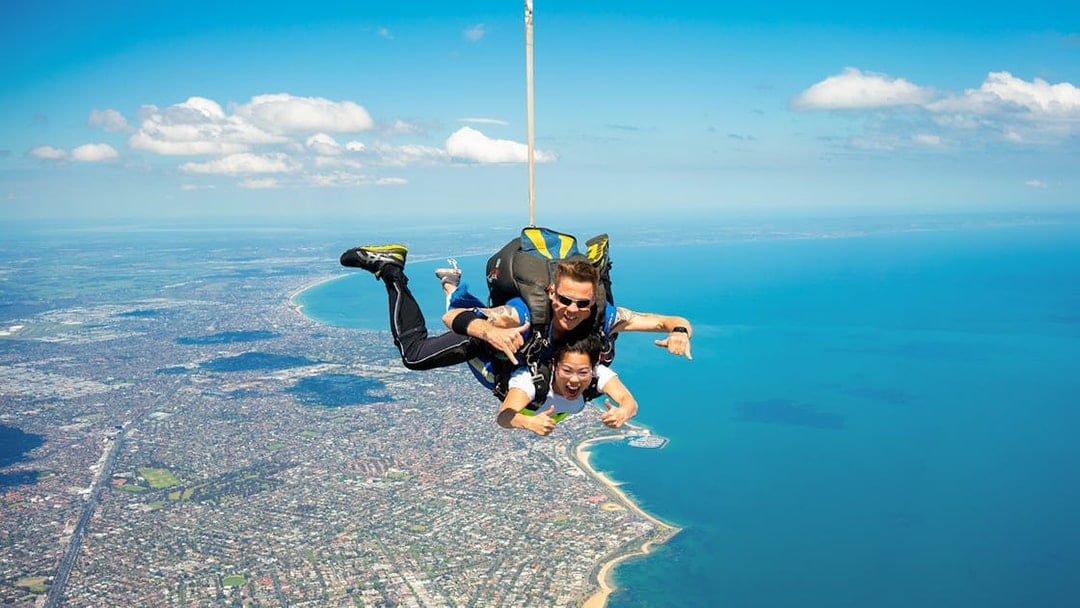 Tandem skydivers over St Kilda Beach, Melbourne with coastline view.