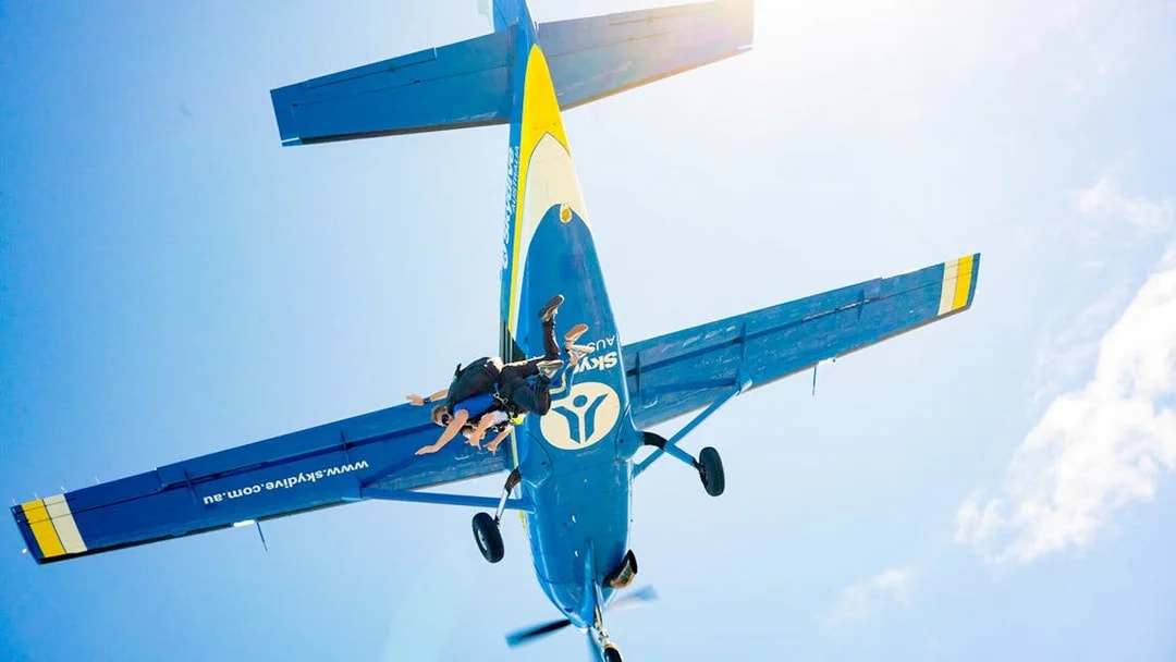 Skydivers jumping from a plane over Melbourne against a clear blue sky.