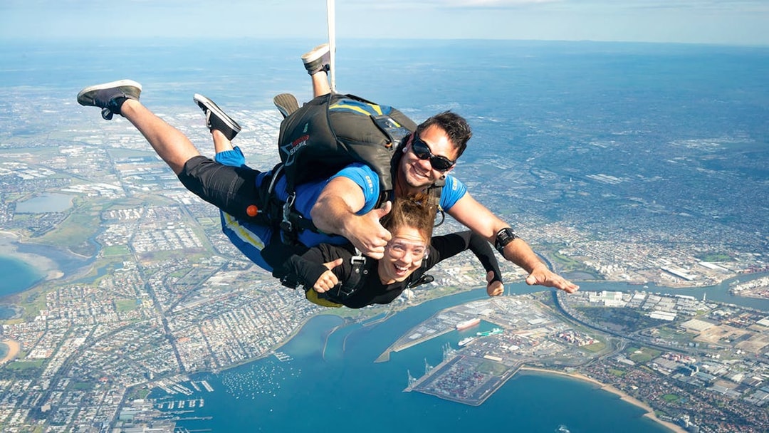Tandem skydivers over St Kilda Beach, Melbourne with city and coastline below.
