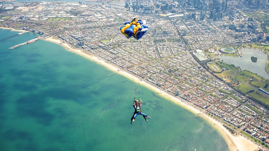 Tandem skydive over St Kilda Beach, Melbourne with cityscape in background.