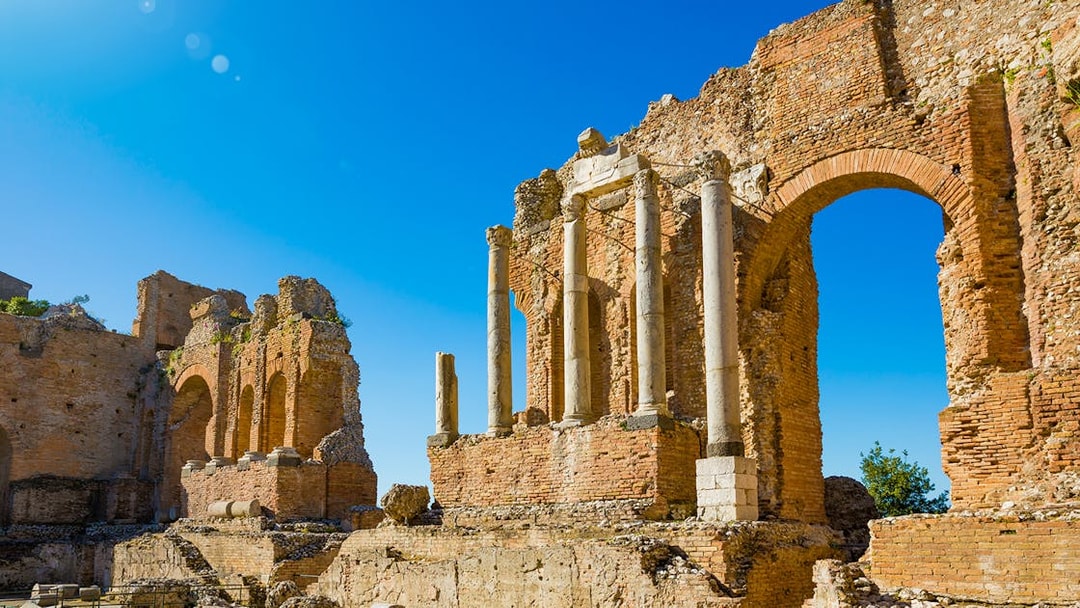 Taormina Ancient Theatre ruins with stone arches and columns under a clear blue sky.
