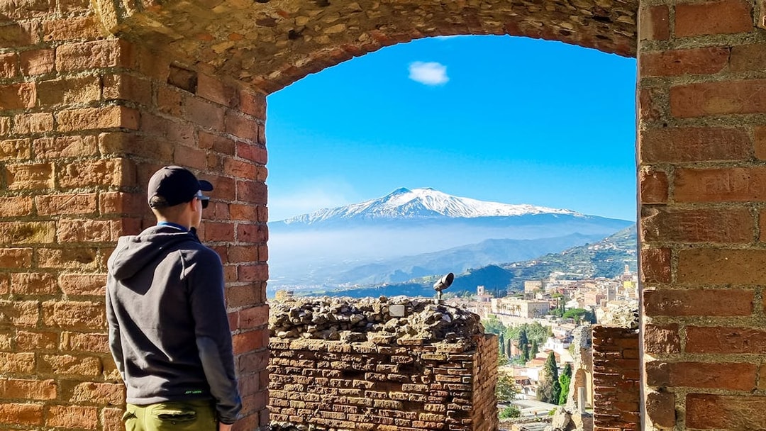 Person viewing Mount Etna through Taormina Ancient Theatre archway, Sicily.