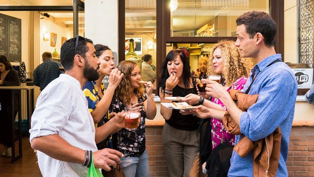 Group enjoying tapas and drinks outside a bar in Seville during a tasting tour.