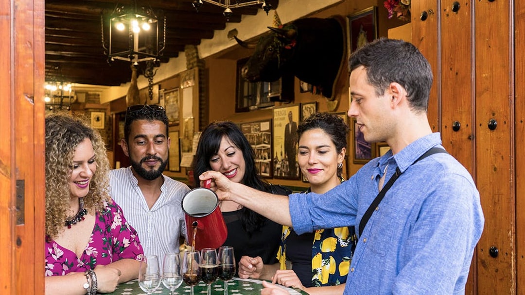 Group enjoying a tapas tasting tour in Seville, with drinks being poured at a local bar.