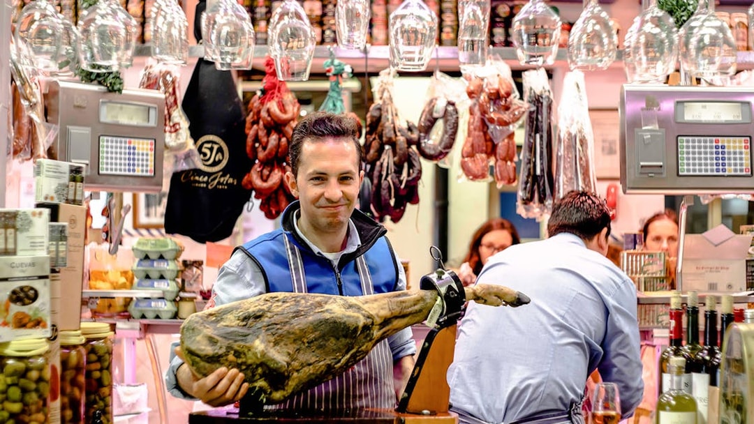 Man presenting cured ham at a tapas bar in Seville during a tasting tour.