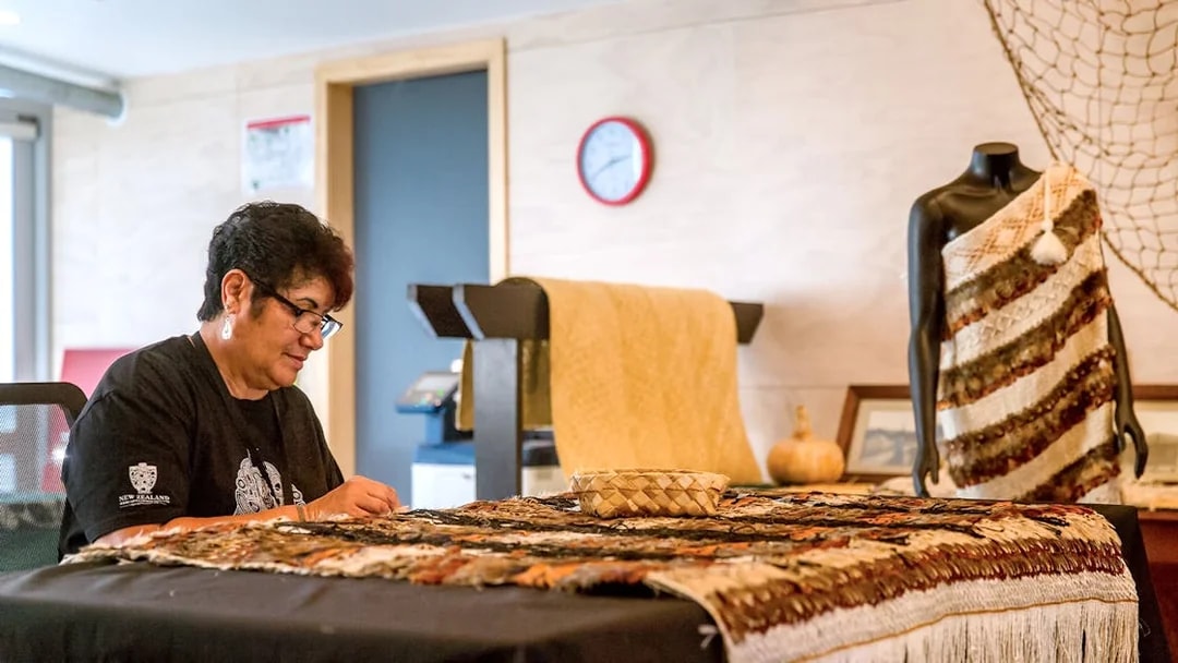 Craftsperson weaving traditional Māori garment at Te Puia, New Zealand.