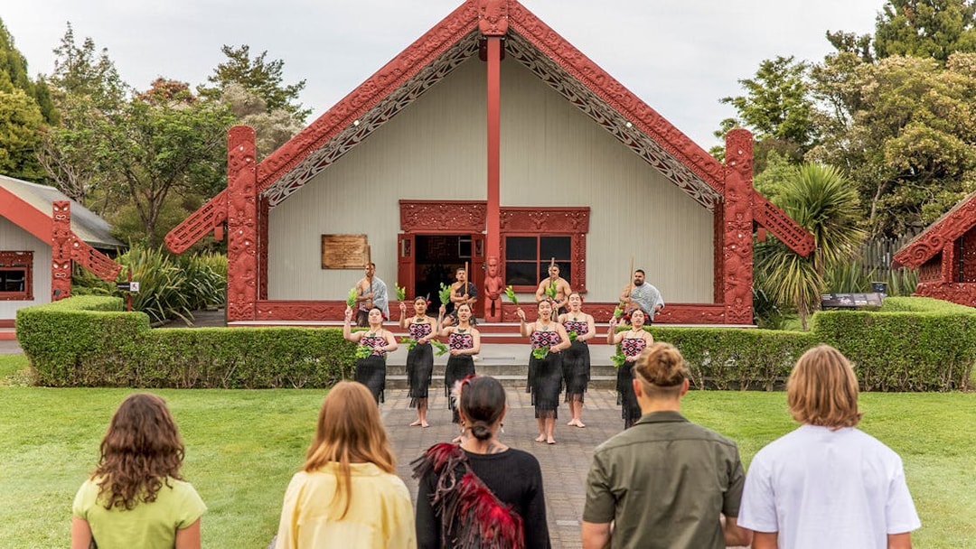 Maori cultural performance at Te Puia, New Zealand, with traditional meeting house in background.