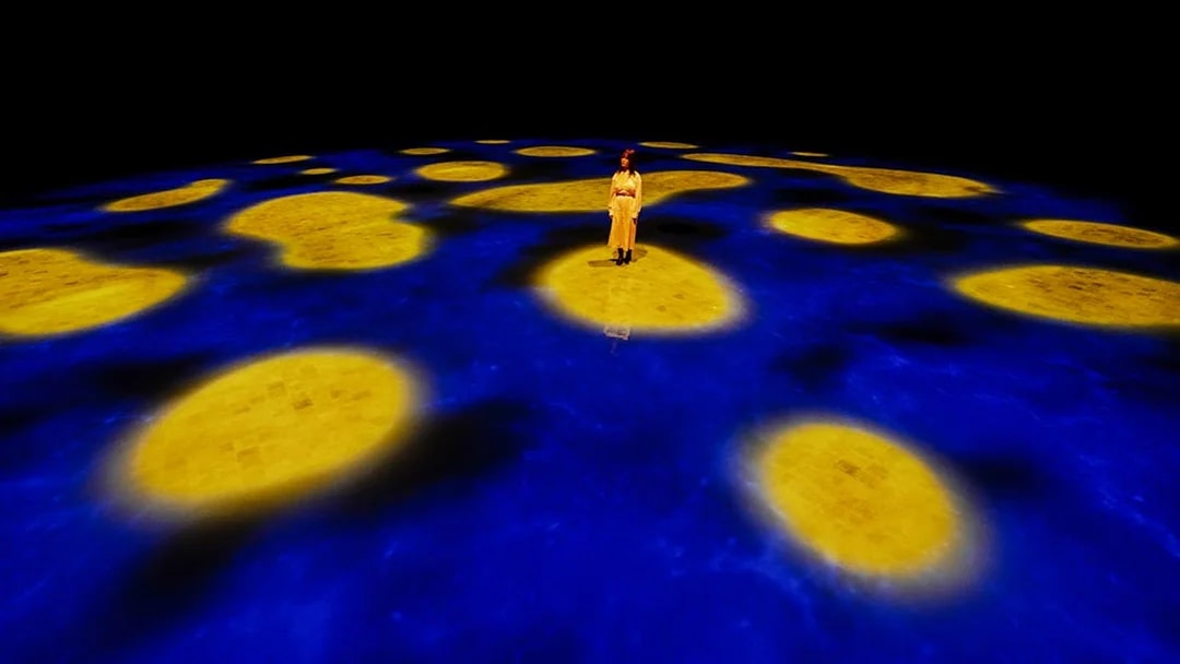 Person standing on illuminated blue and yellow interactive floor at Team Lab Abu Dhabi.