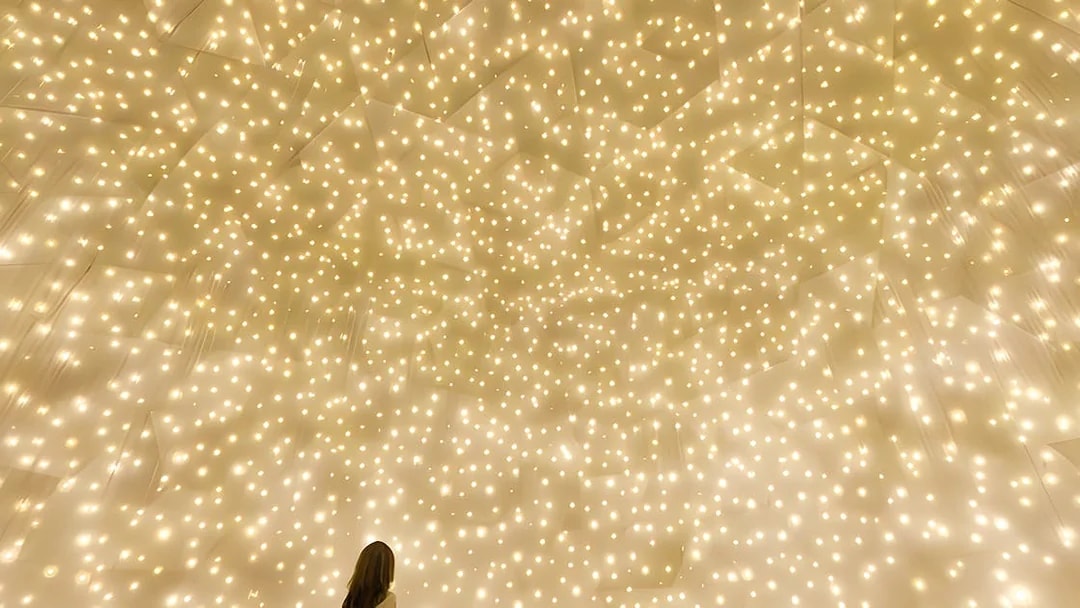 Person gazing at illuminated installation at TeamLab Phenomena Abu Dhabi.