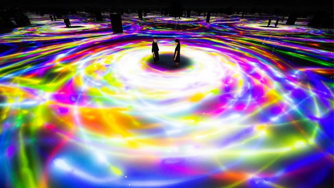 Visitors at TeamLab Planets Tokyo surrounded by swirling colorful digital light displays.