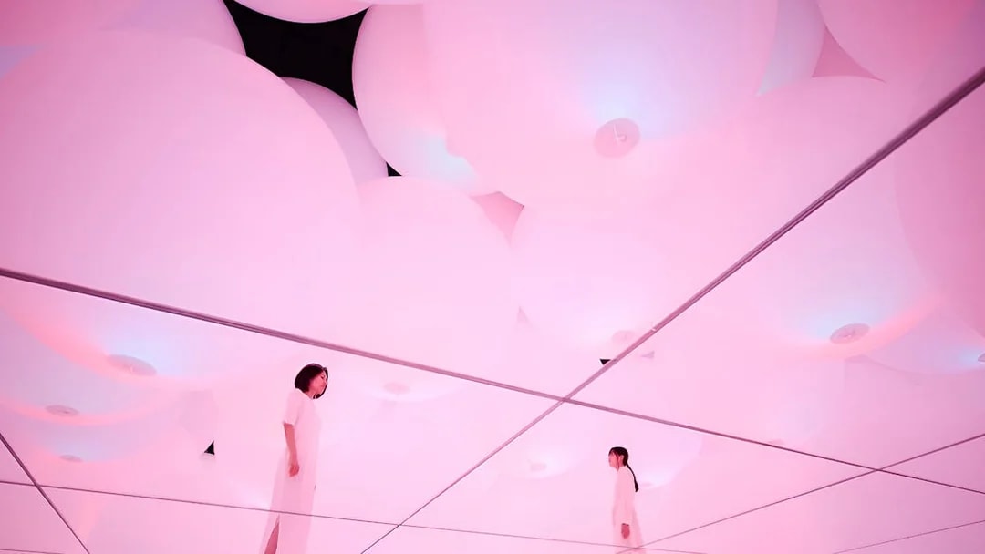 Visitors in mirrored room with pink digital light at TeamLab Planets Tokyo exhibit.