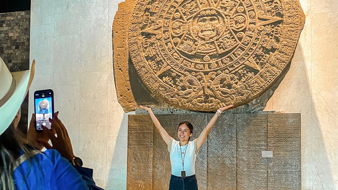 Stone Aztec calendar at the Anthropology Museum, Mexico, with a visitor posing in front.