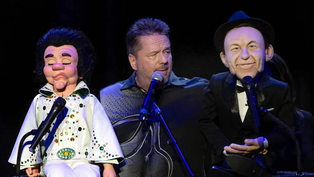 Ventriloquist performing with Elvis and Frank Sinatra puppets on stage.